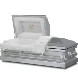 A silver casket is open, revealing a white cushioned interior with an embroidered design on the inside of the lid. A textured white blanket is draped over the edge.