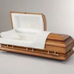 A wooden casket with a partially open lid displays a white cushioned interior, a white pillow, and a white blanket draped over the side, set against a plain light background.