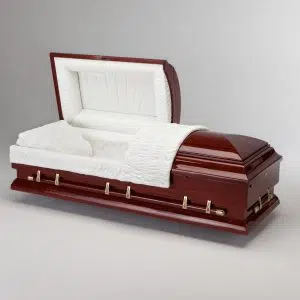 A polished wooden casket with an open lid, lined with white cushioned fabric and a matching pillow and blanket, positioned against a plain light gray background.