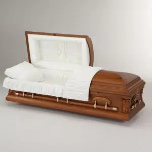 A wooden casket with metal handles is shown open, revealing a white cushioned interior with a pillow and fabric lining, set against a plain light background.