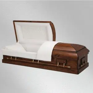 A wooden casket with brass handles and a white cushioned interior is open, showing the lining and pillow inside. The casket is displayed against a plain light gray background.